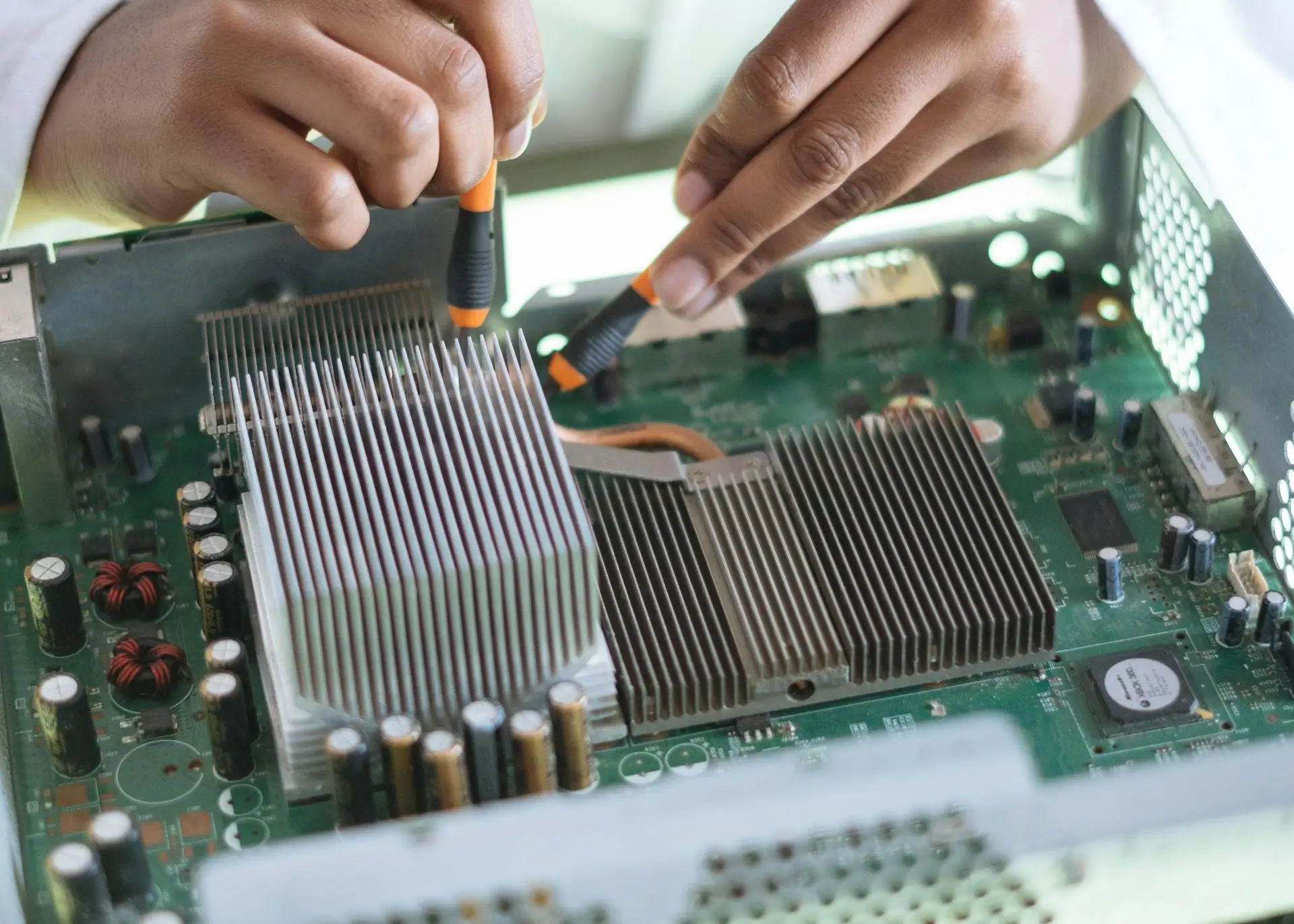 A person uses tools to work on a computer motherboard, adjusting the heatsink inside a metal casing. The image shows a close-up of their hands focusing on electronic components and connections.